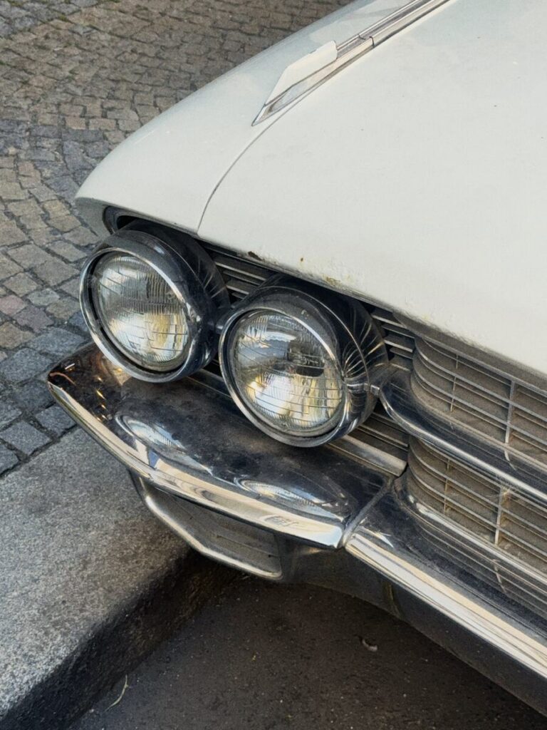 Twin headlights of an old white car on cobblestones