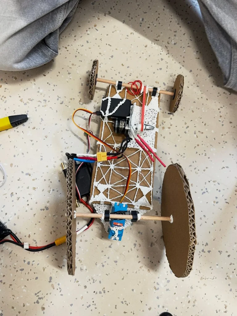 Top view of a cardboard chassis reinforced with a web drawn with a 3D pen, with motor, wiring and cardboard wheels
